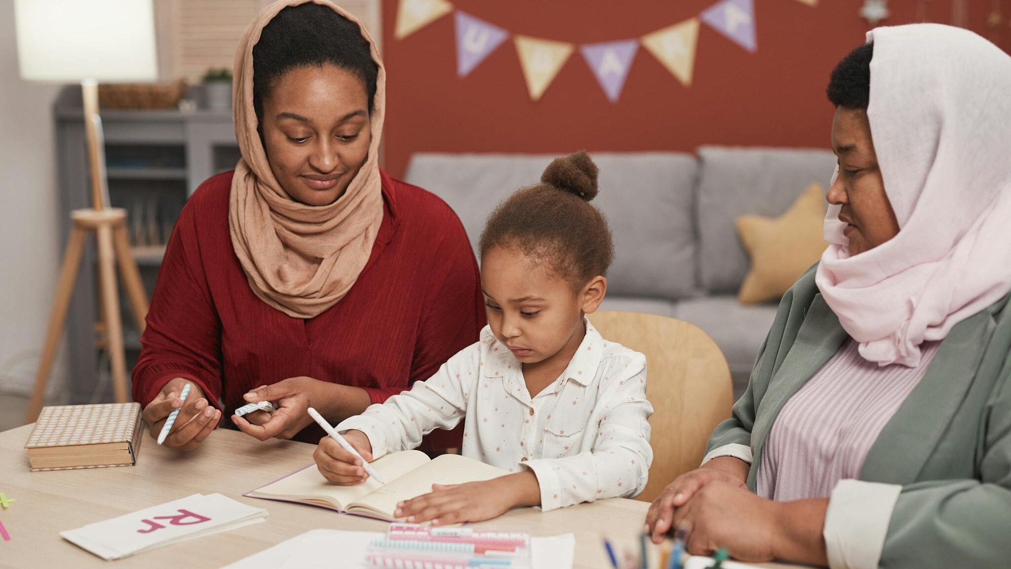 A child learning and drawing with two adults guiding her in an indoor setting.
