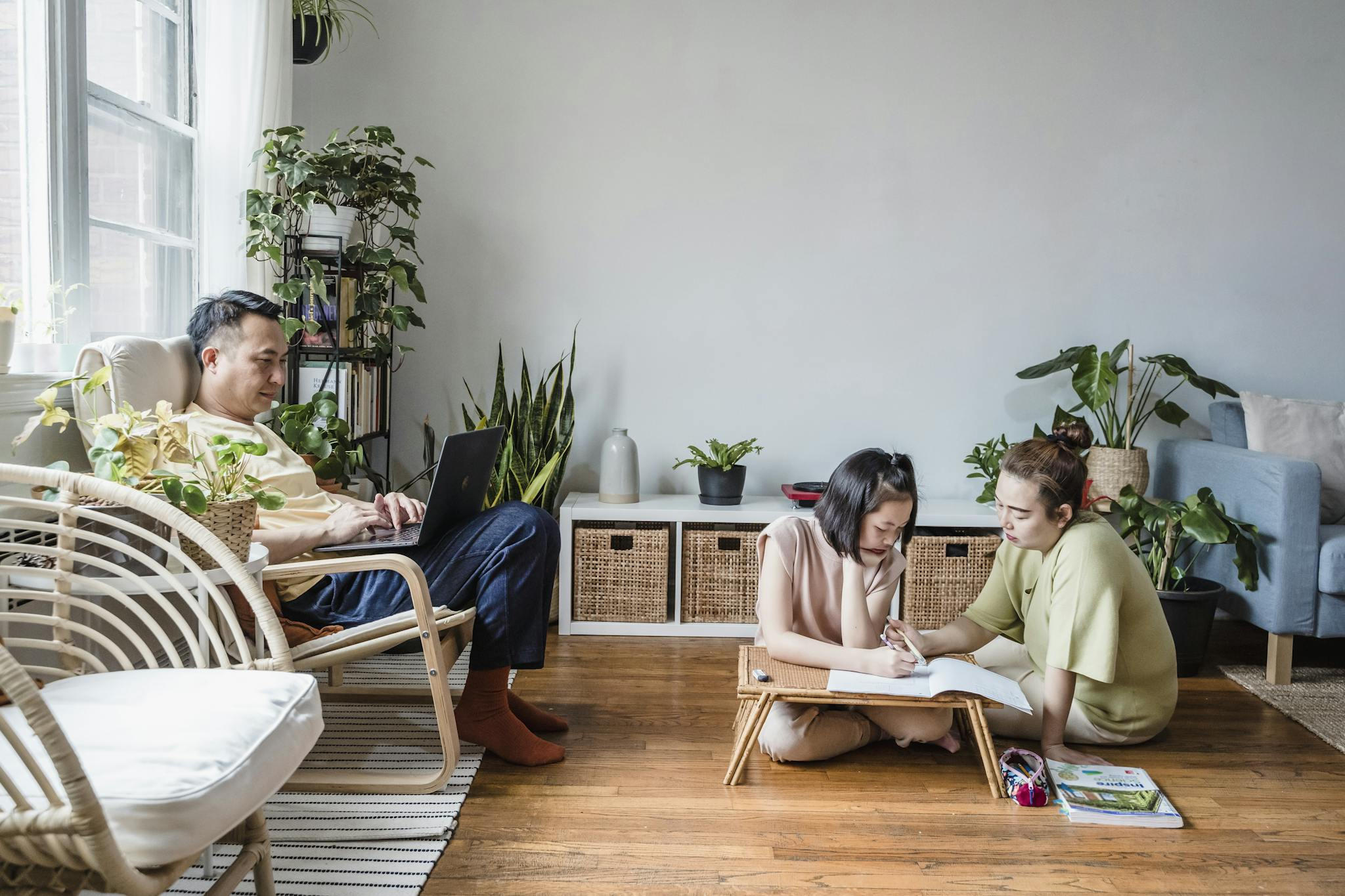 A family engaged in home study with dad on a laptop and mom helping daughter with homework.